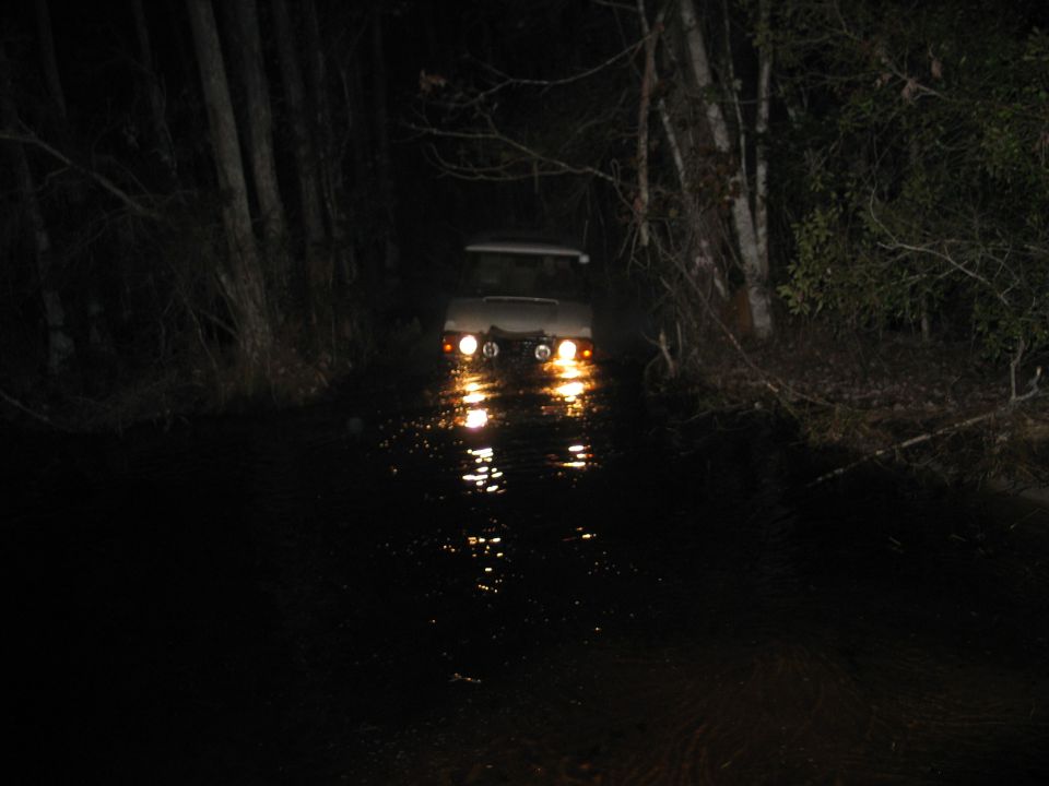 SUV with round driving lights wading a flooded path at night, lights reflecting on water