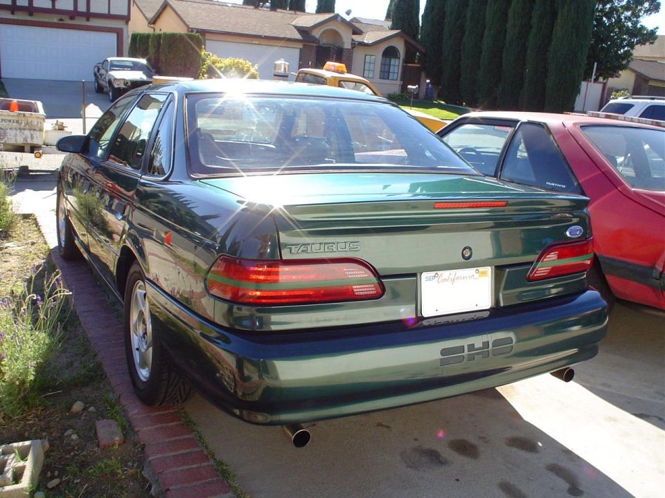 Green sedan with a spoiler and dual exhaust pipes, parked on a driveway