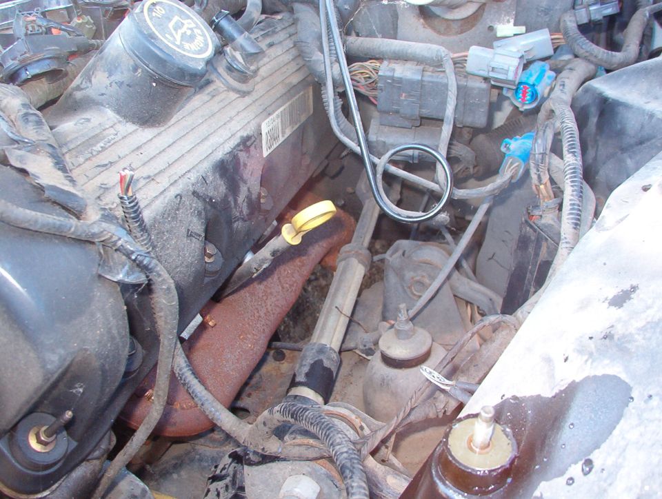 Engine bay close-up with rusty exhaust manifold, yellow dipstick, and wiring harnesses