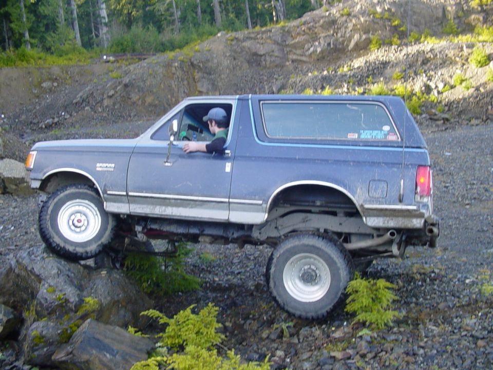 Driver leaning out window of a lifted gray two-door Ford Bronco parked in a rocky quarry