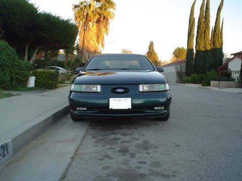 1993 Ford Taurus - Front view of a dark green 1993 Ford Taurus parked curbside on a street.