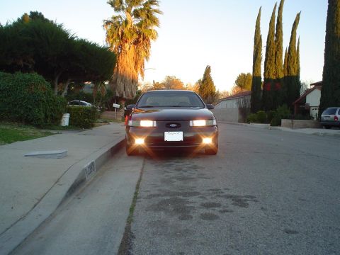 1993 Ford Taurus - A dark colored 1993 Ford Taurus is parked on the street in front of a house with palm trees in the background.