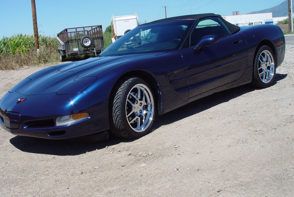 Dark blue Corvette convertible with chrome wheels on gravel lot