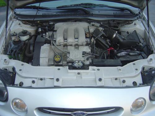 Open engine bay of a silver Ford showing a transverse V6 engine and front grille emblem