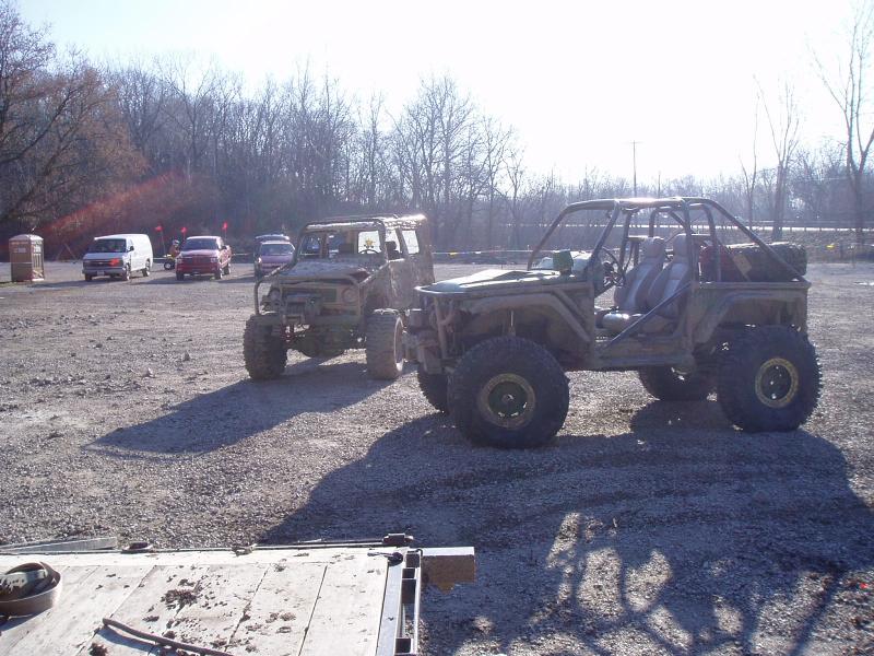 Two heavily modified off-road vehicles with large tires and roll cages parked on a gravel lot