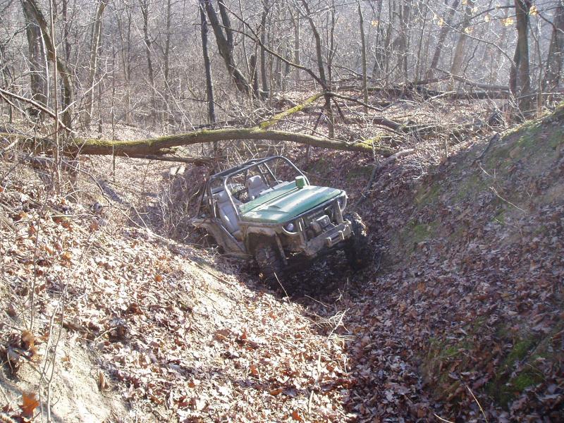 Green off-road vehicle navigating a steep, leaf-covered ditch