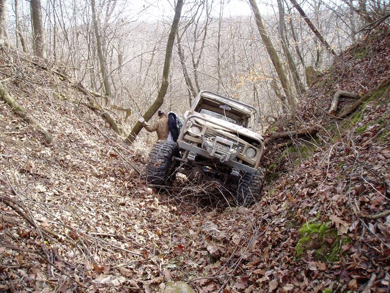 Off-road vehicle struggling on a steep, leaf-covered slope in a forest