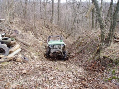 1992 Ford Bronco - Off-road vehicle descends a steep, wooded trail with fallen leaves and logs.