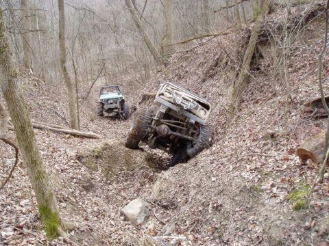 1992 Ford Bronco - Two off-road vehicles navigate a challenging, wooded ravine during an excursion.