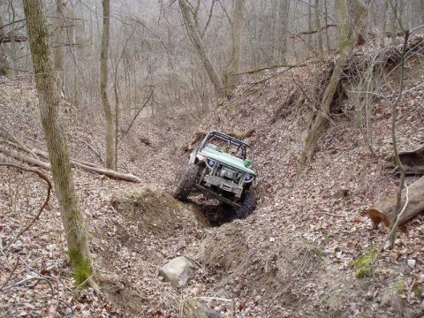 1992 Ford Bronco - An off-road vehicle navigates a challenging, wooded ravine with steep, leaf-strewn sides.