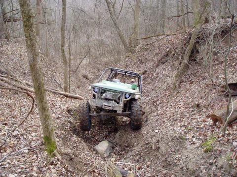 1992 Ford Bronco - This off-road buggy is shown navigating a challenging, narrow trail through a wooded area.