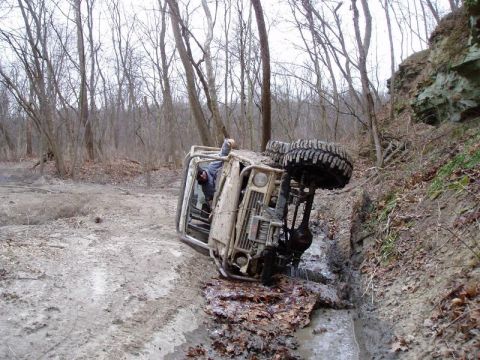 1992 Ford Bronco - An off-road vehicle has overturned on a muddy trail, its wheels in the air.