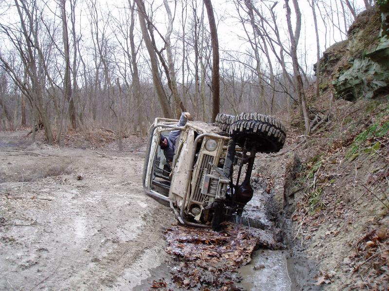 Mud-covered off-road vehicle overturned on a muddy trail next to a rocky embankment