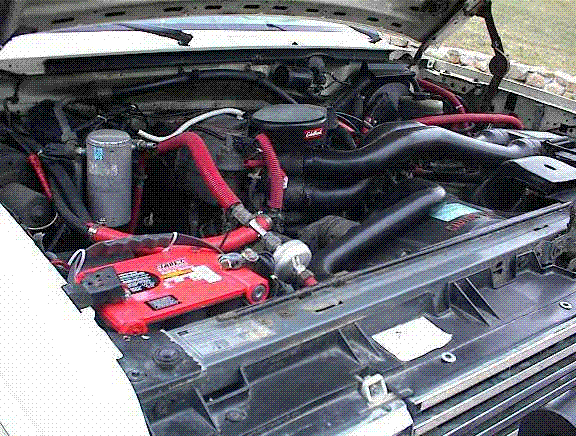 Engine bay of a 1988 Ford Bronco with red battery, red hoses, and Edelbrock air cleaner