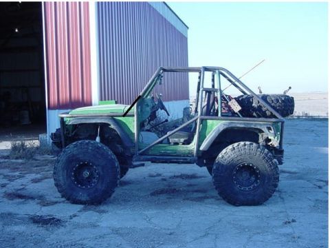 1992 Ford Bronco - Modified 1992 Ford Bronco with custom roll cage and off-road tires parked outside a building.