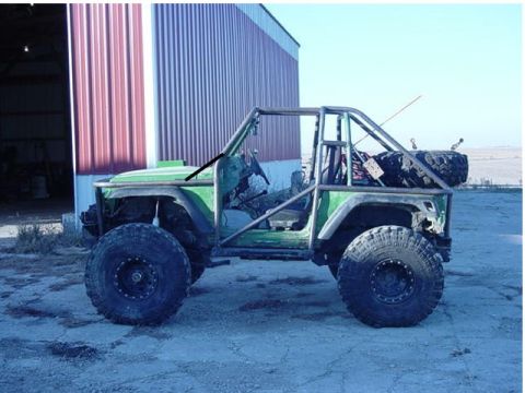 1992 Ford Bronco - A heavily modified off-road vehicle with a custom roll cage and large tires sits outside a barn-like structure.