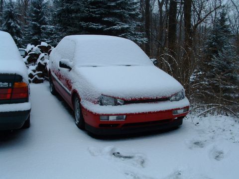1994 Volkswagen Jetta - A red Volkswagen Jetta is covered in snow, parked next to another vehicle in a wooded area.