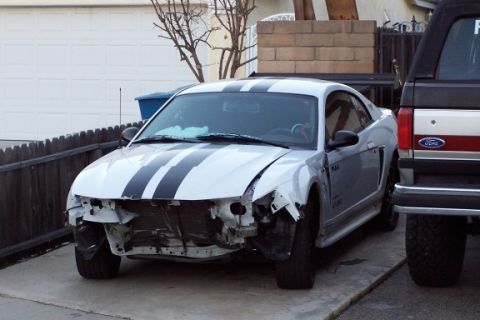 1990 Ford Bronco - This white coupe, possibly a Ford Mustang from the early 2000s, is missing its front bumper and grille, parked beside a Ford truck.