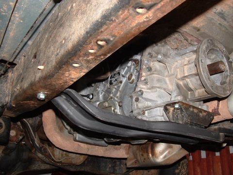 1990 Ford Bronco - Underside view of a vehicle drivetrain showing the transmission, transfer case with output shaft and a frame crossmember.