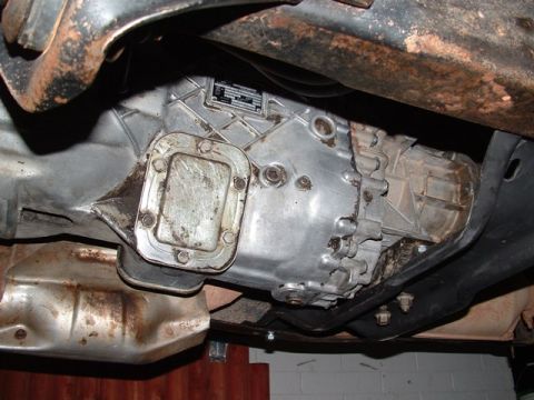 1990 Ford Bronco - Underside view of a transmission or transfer case housing, showing a bare aluminum casing with a bolted-on square cover plate, mounting bol…