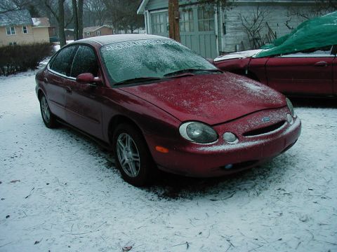 1997 Ford Taurus - A maroon sedan sits in a snowy yard next to another vehicle covered by a green tarp.