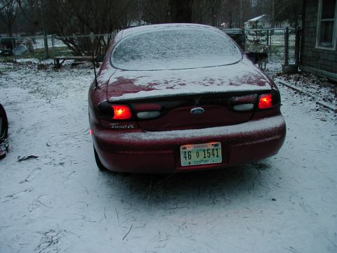 1997 Ford Taurus - Rear view of a 1997 Ford Taurus covered in snow with brake lights on.