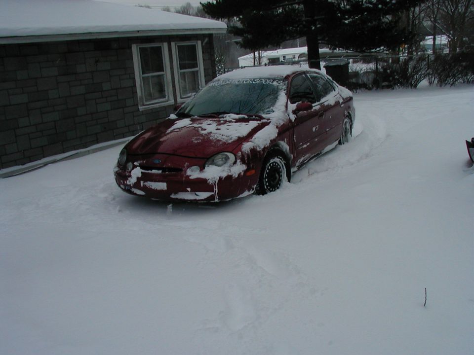Red 1997 Ford Taurus partially buried in snow, front 3/4 view
