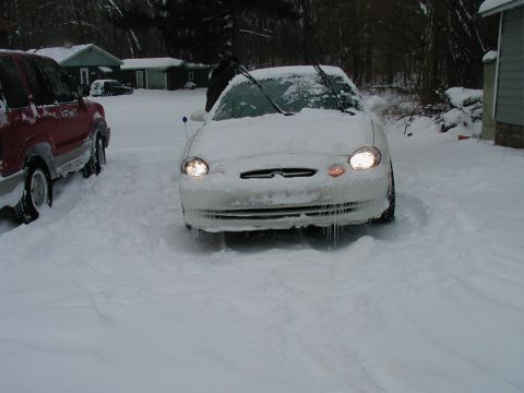 1997 Ford Taurus - A white sedan is partially buried in snow with icicles hanging from its front bumper.
