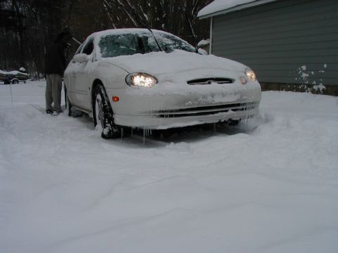 1997 Ford Taurus - A white 1997 Ford Taurus is partially buried in snow with icicles hanging from its front bumper.