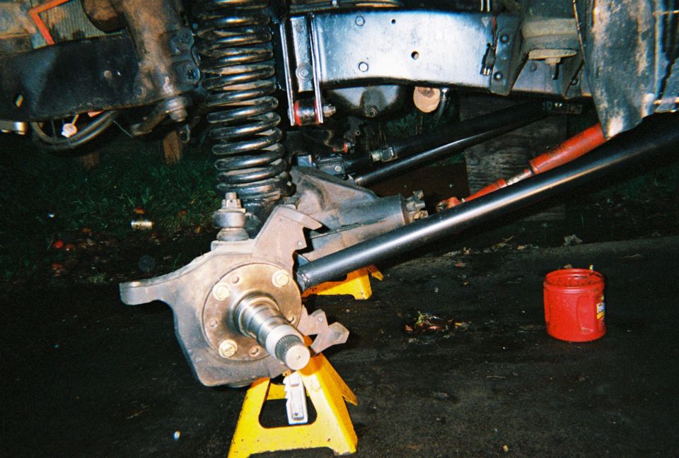 Front axle knuckle and spindle on a yellow jack stand under a vehicle at night