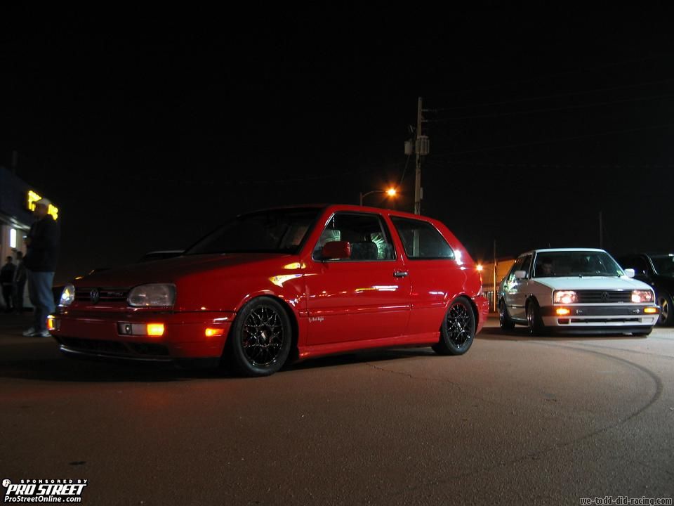 Red 1993 Volkswagen Golf GTI parked next to a white Volkswagen Golf GTI at night
