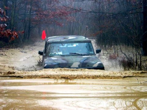 1979 Ford Bronco - A camouflaged SUV navigates through a deep mud puddle on a trail.
