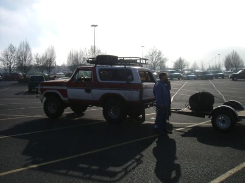1993 Ford Bronco - A red and white Ford Bronco from the late 1970s is parked in a lot, hitched to a trailer.