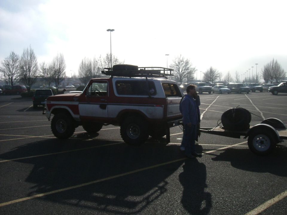Red and white Ford Bronco with roof rack and spare tire, towing a trailer with a spare tire