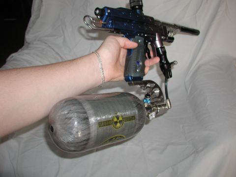 1985 Ford Bronco - A paintball gun and air tank are held by a person's hand against a white background.