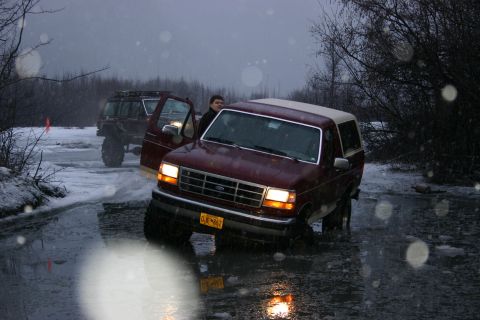 2003 Jeep TJ - Two SUVs navigate icy conditions, with one Ford Bronco appearing stuck in the water.