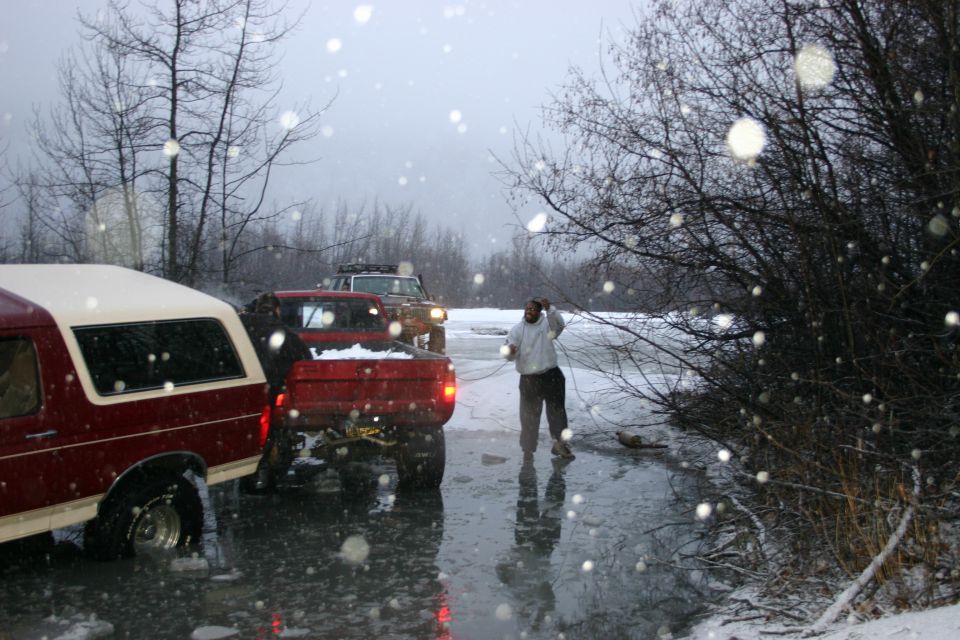 Red pickup truck and maroon SUV stuck on ice, with a person standing nearby
