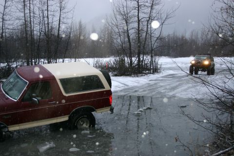 2003 Jeep TJ - Two SUVs navigate a snowy, icy landscape, with one vehicle partially submerged in water.