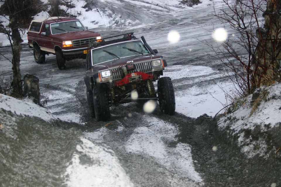 Maroon Jeep Cherokee XJ and red Ford Bronco driving on a muddy, snowy trail