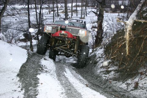 2003 Jeep TJ - A heavily modified Jeep Cherokee XJ navigates a challenging off-road trail in a snowy, wooded environment.