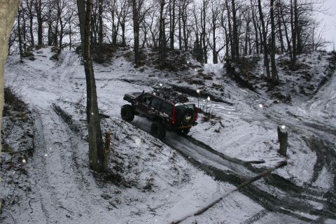 2003 Jeep TJ - An off-road SUV navigates a challenging, snowy, and muddy incline.