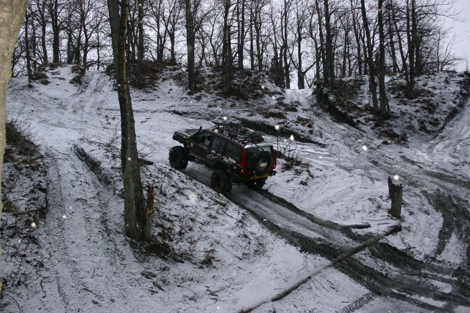 Dark SUV with roof rack and large tires driving on a muddy, snow-covered hill