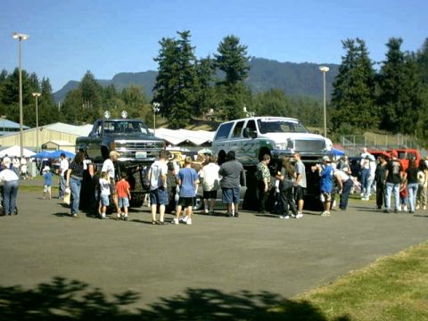 1995 Ford Bronco - A gathering of people surrounds two large, lifted trucks at an outdoor event.
