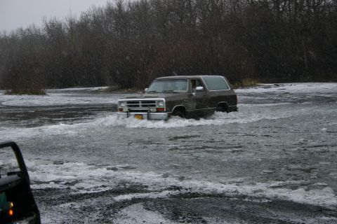 2003 Jeep TJ - A brown SUV navigates through icy water, with a portion of another vehicle visible in the lower left corner.