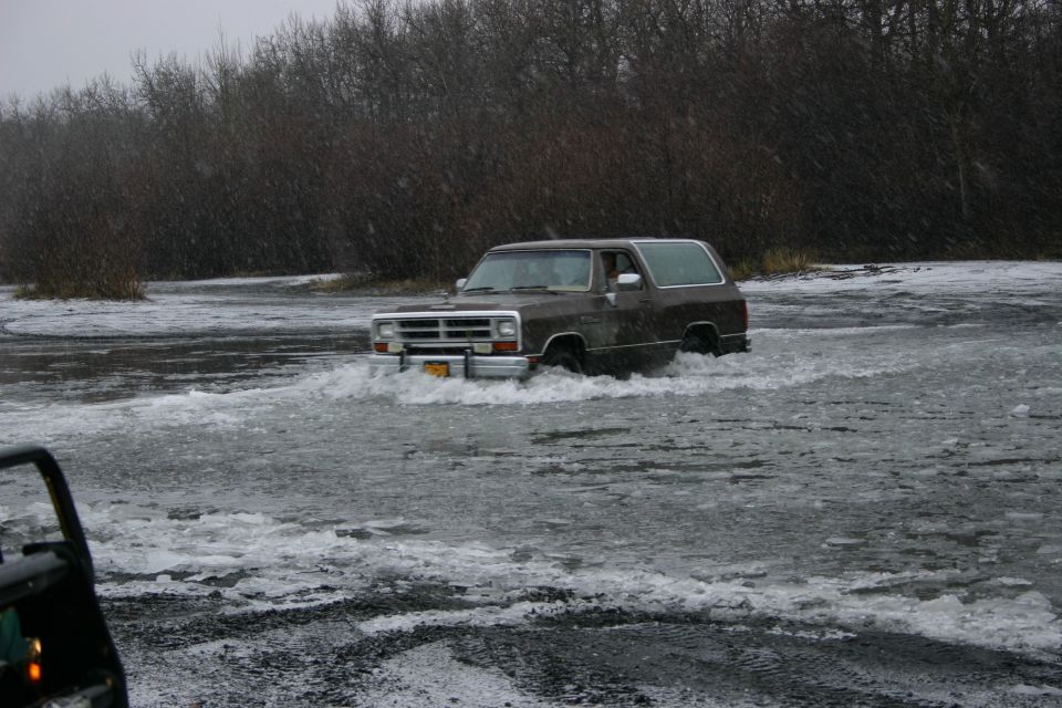 Brown SUV with a chrome grille driving through icy water, with another vehicle partially visible in the foreground