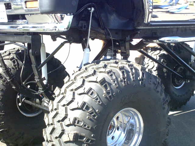 Underside of lifted truck: solid front axle, leaf springs, shocks and mud tires on chrome wheels