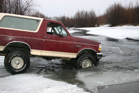 2003 Jeep TJ - Ford Bronco navigates icy water in a snowy landscape.