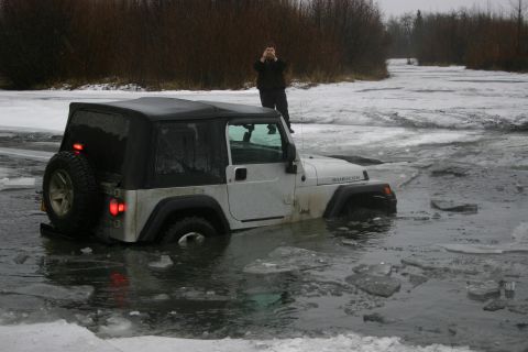2003 Jeep TJ - A silver 2003 Jeep Wrangler Rubicon is partially submerged in icy water, with a person standing on its roof taking a picture.