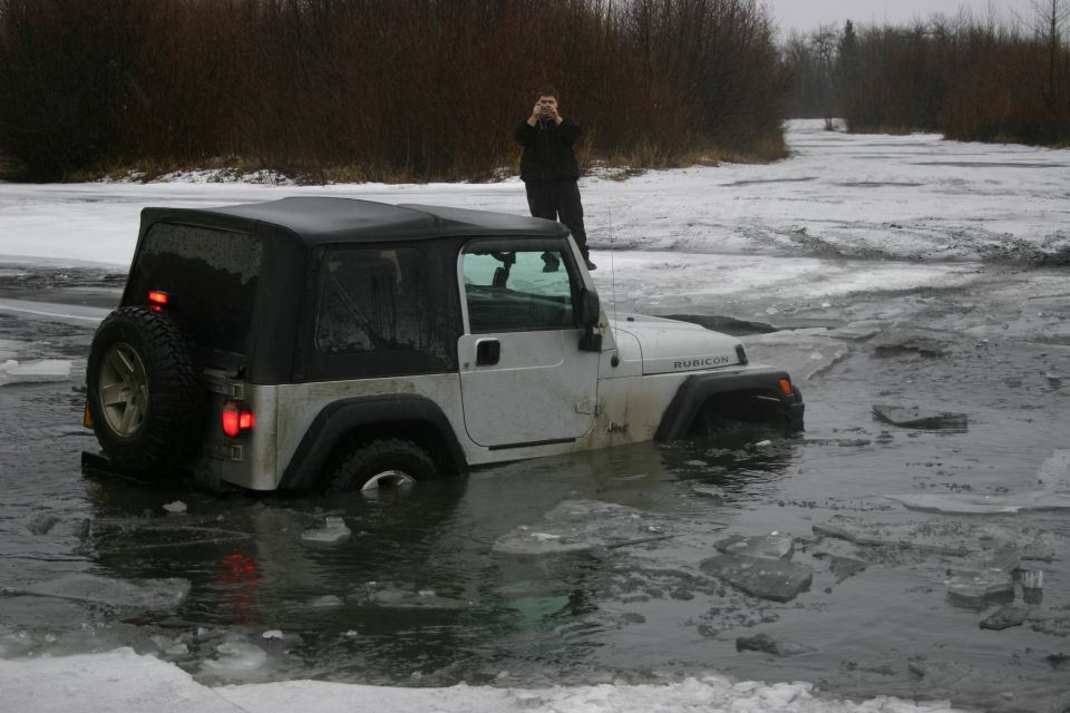 Silver 2003 Jeep Wrangler Rubicon stuck in icy water with a person on top taking a photo