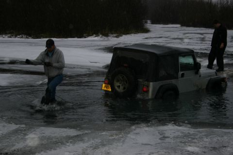 2003 Jeep TJ - A Jeep Wrangler is partially submerged in icy water with a person attempting to free it.